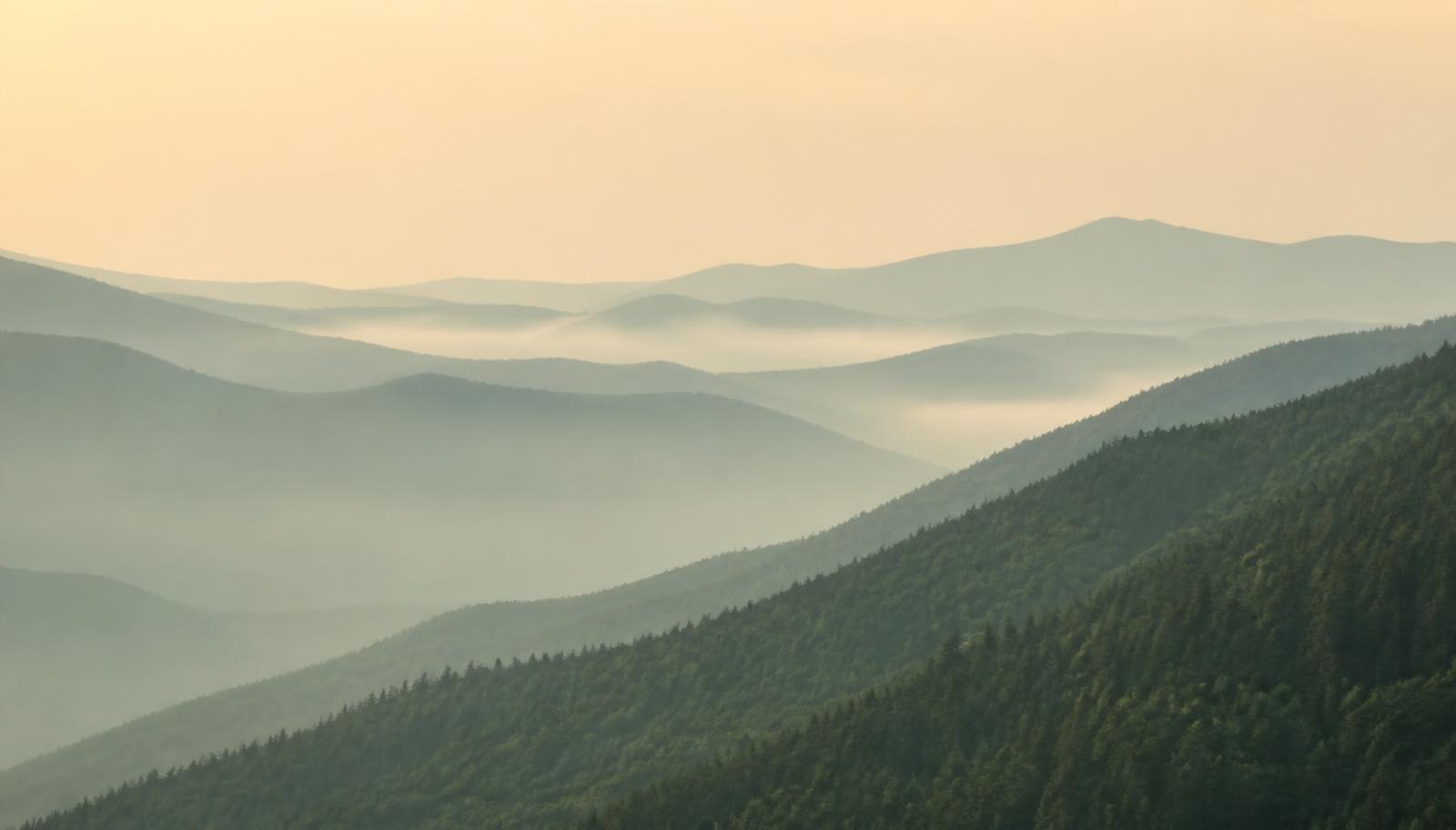 Layered green mountain ridges in soft morning mist